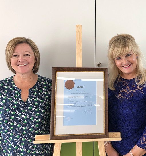 two females standing next to framed taught degree awarding powers certificate