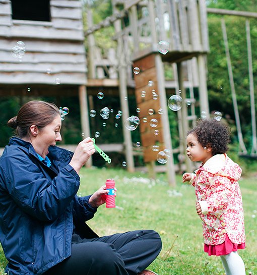 female student and little girl blowing bubbles in garden