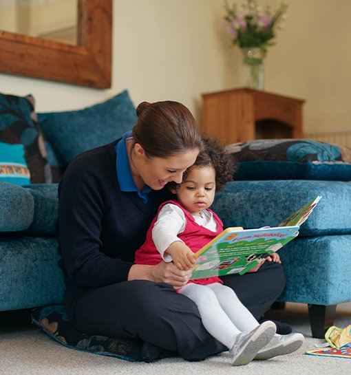 a female Norland Nanny reading a book with a child