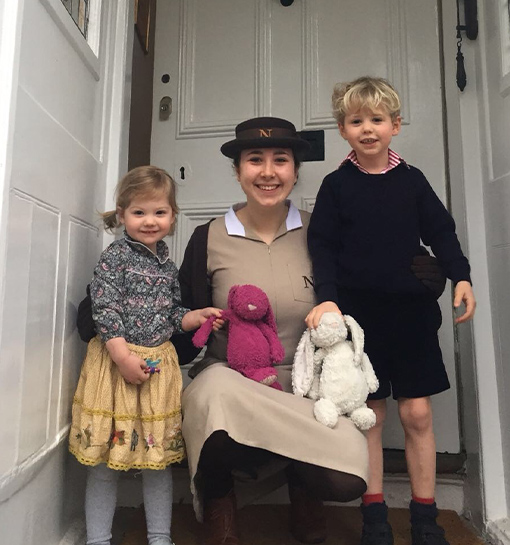 female Norland nanny in uniform on door step in-between two children