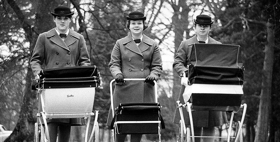three norland nannies in uniform pushing silver cross carriage prams down the street