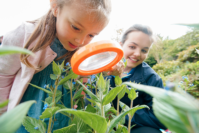 female student and girl in the garden looking through magnifying glass