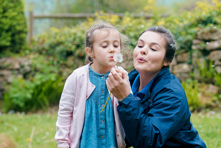 female student and girl blowing dandylion in garden