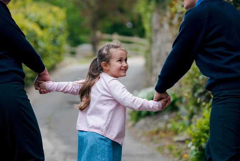 young girl holding hands of two adults