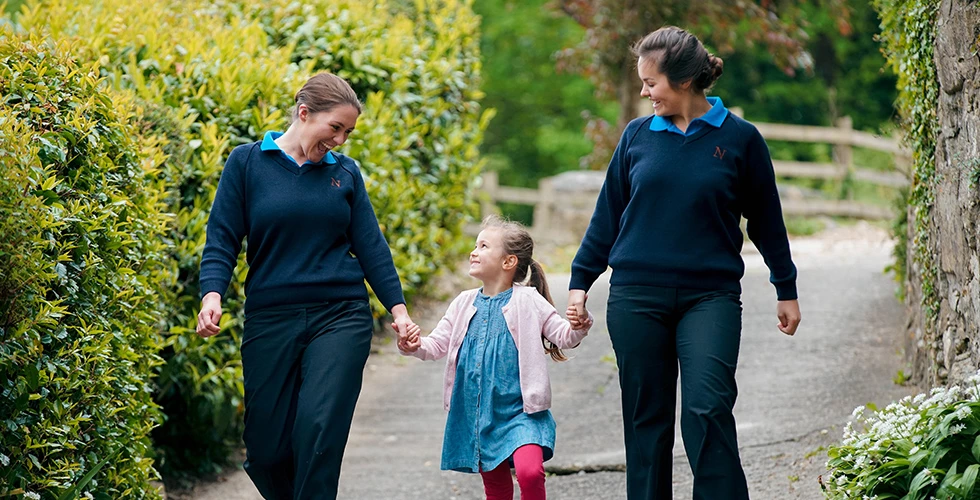 girl holding hands of two female students walking down path
