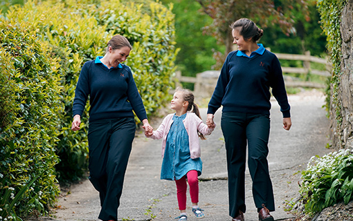 girl holding hands of two female students walking down path