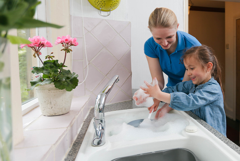 female student and young girl washing up in kitchen looking at bubbles