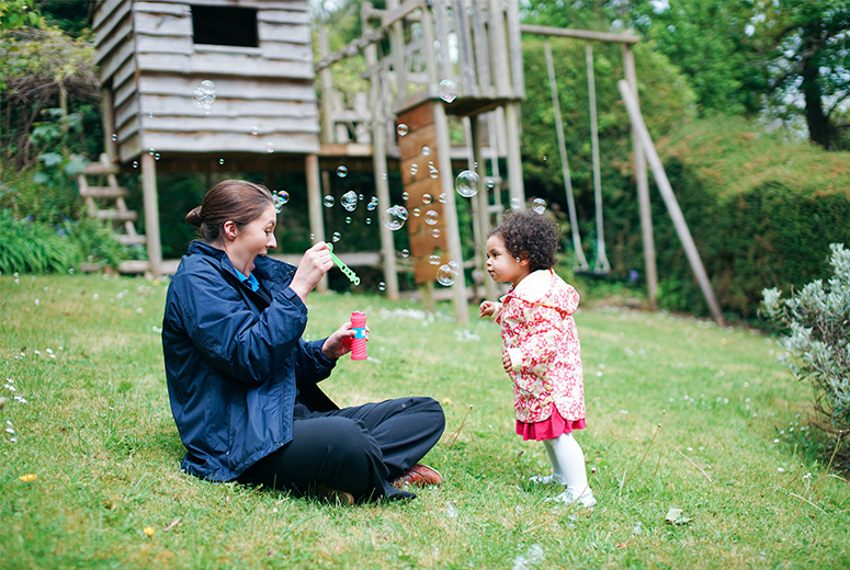 female student training to be an early years practitioner and little girl blowing bubbles in garden
