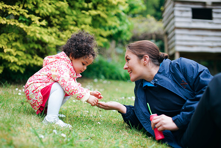 female nanny and little girl playing with daisies in garden