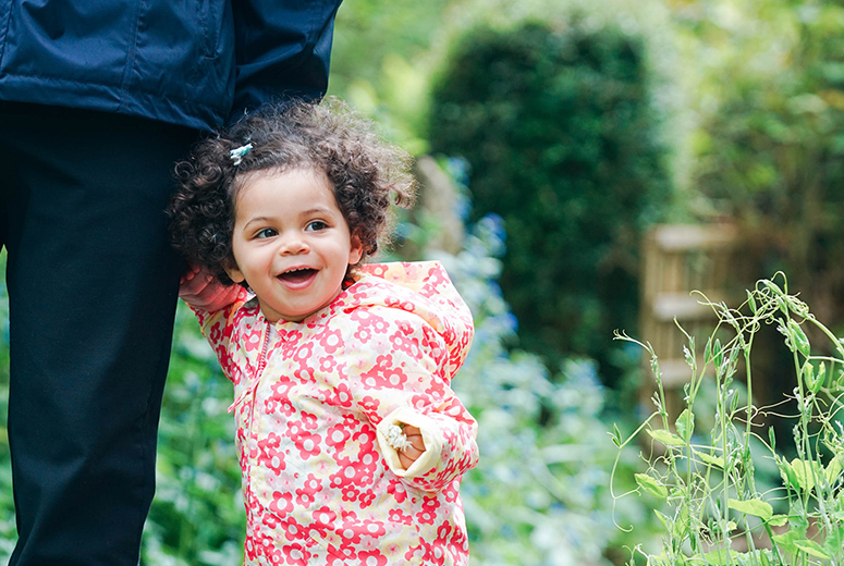 little girl in flowery coat holding adult's hand smiling