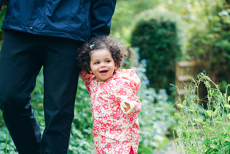 little girl in flowery coat holding adult's hand smiling