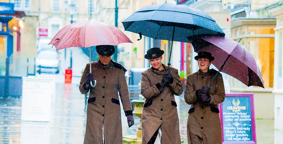 three Norland nannies walking down street in the rain with umbrellas