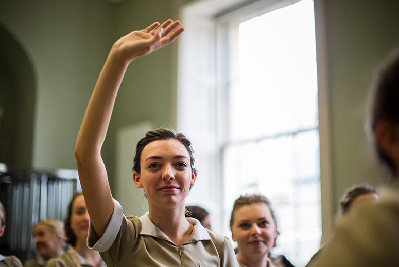 female raising hand in lecture to ask a question