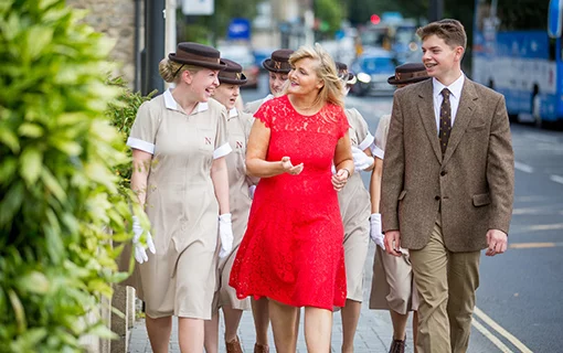 group of Norland nannies in uniform walking with female in red dress down the street