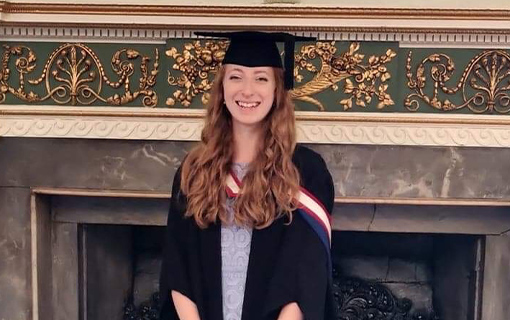 a female student in her graduation robes smiling
