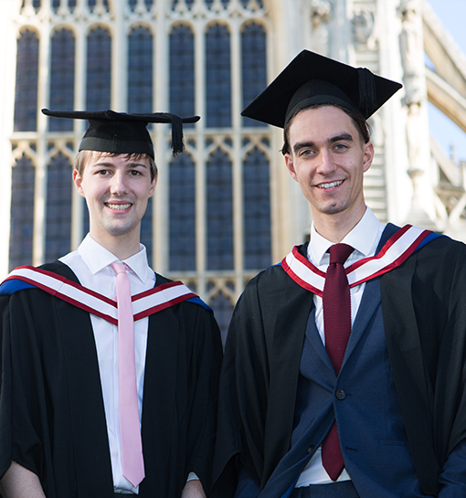 two male nannies graduating outside bath abbey wearing mortarboard and gown