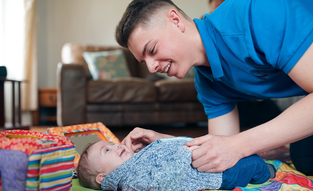 a male student nanny and a baby smiling at each other