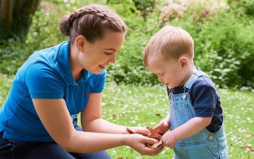 a boy playing with leaves with a student nanny