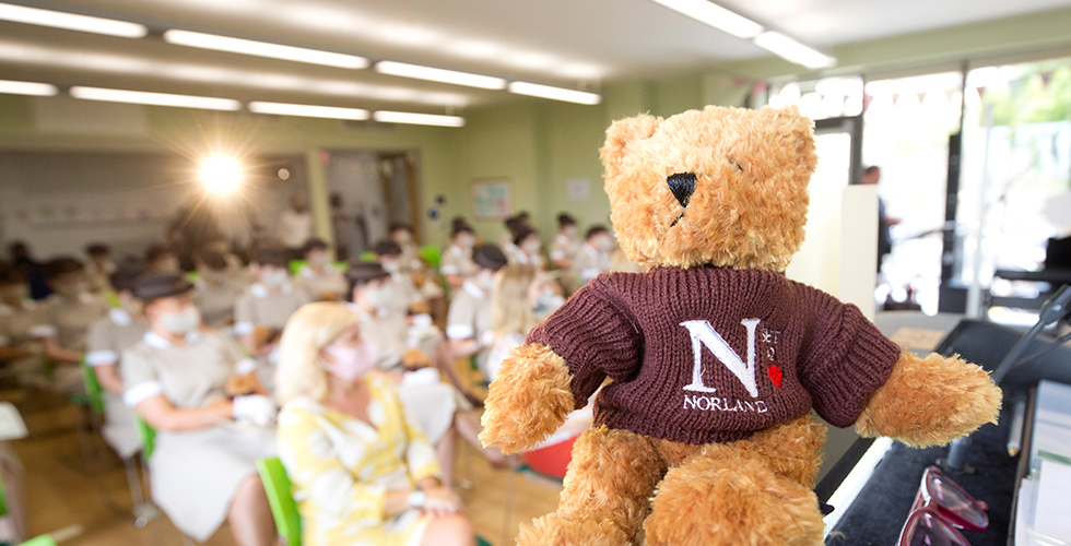 a teddy bear on a plinth in front of a seated audience