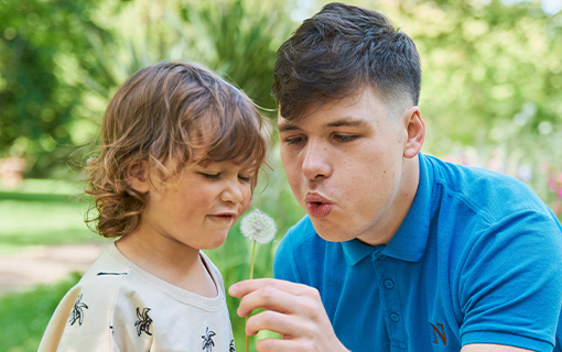 a male Norland student blowing a flower with a little boy