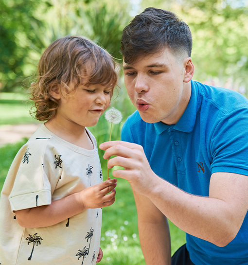 a male Norland student blowing a flower with a little boy