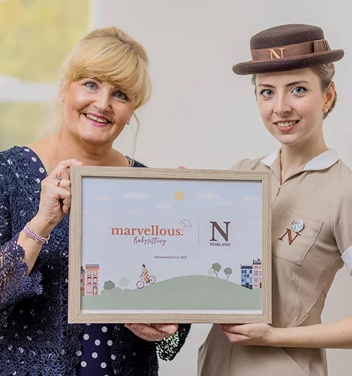 Two females holding a frame announcing the launch of a new babysitting app