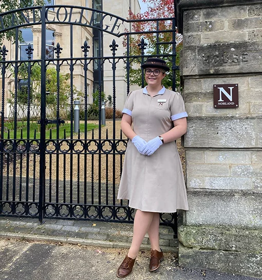 a female Norland Nanny student in uniform outside gates