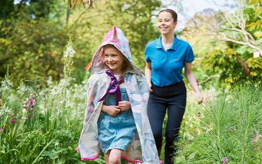 a girl wearing a cape smiling with a female Norland Nanny student