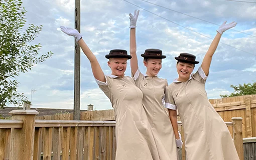 three students in uniform smiling with their hands in the air