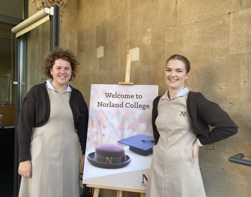A Norland Nanny and a student smiling in front of a welcome sign