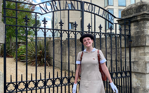 a female Norland Nanny student stood in front of Norland College's gates smiling