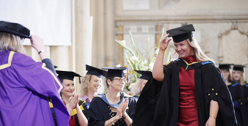 A Norland graduate doffing her cap when on stage at her graduation inside Bath Abbey