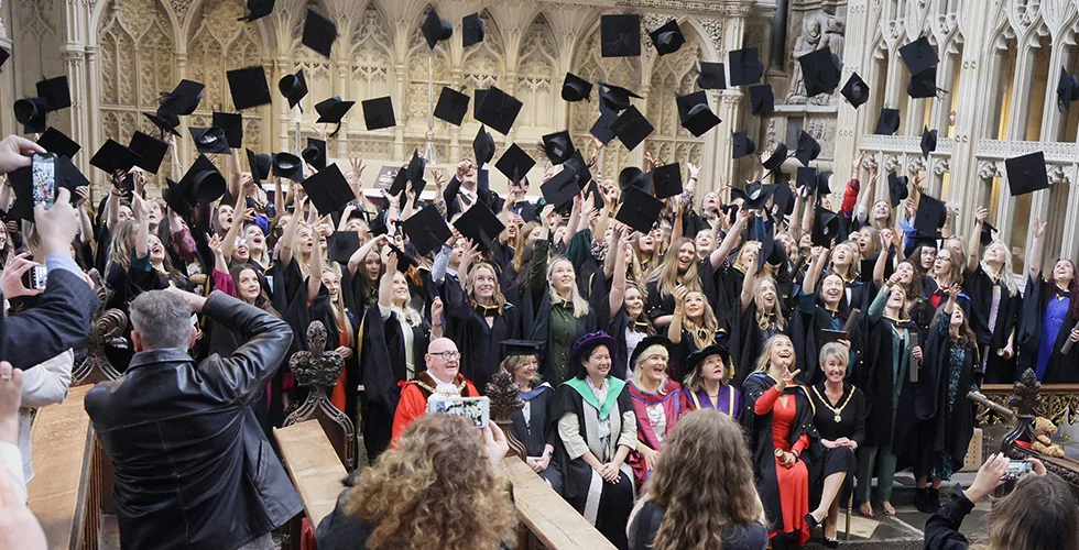 Norland graduates throwing their mortar boards in the air at their graduation in Bath Abbey