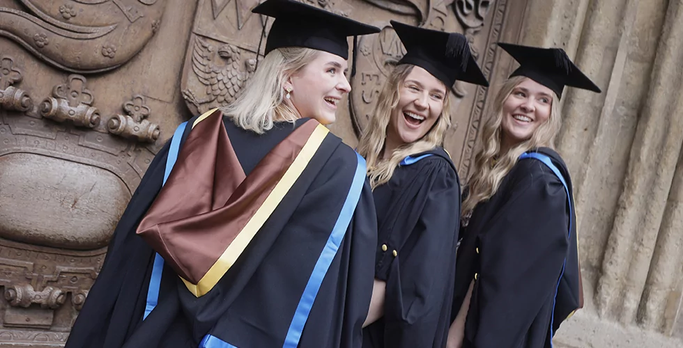 Three Norland graduates smiling outside the Bath Abbey at their graduation ceremony
