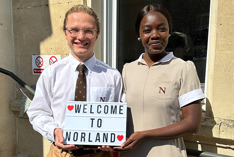 A male and a female Norland Nanny students in their uniform holding a sign saying Welcome to Norland at an open day