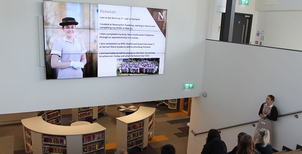 a female student training to become a Norland Nanny delivering a presentation to students at a school.