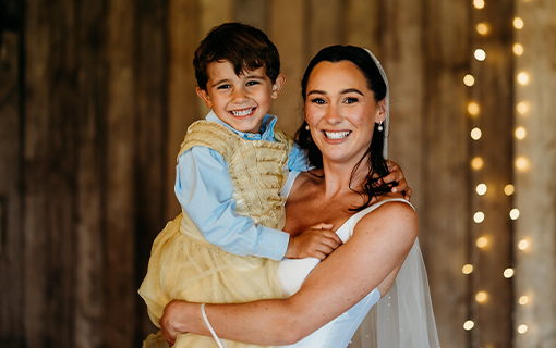 A bride in a white wedding dress holding a child smiling
