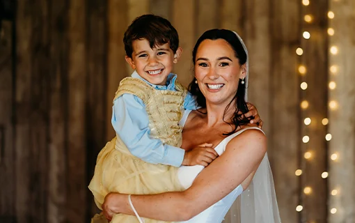 A bride in a white wedding dress holding a child smiling