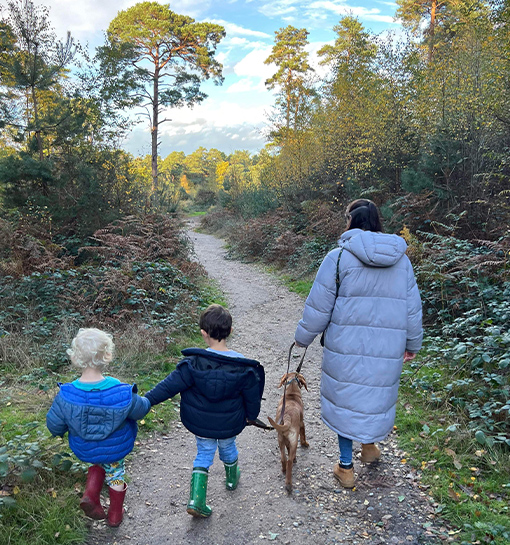 A nanny walking with two children and a dog on a country path.