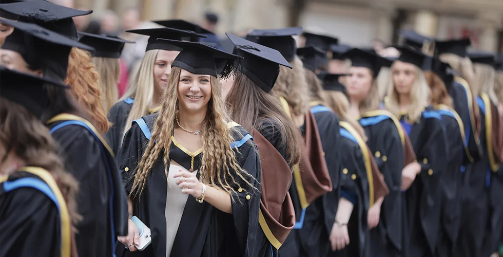 A degree graduate smiling in a queue of graduates outside the Bath Abbey