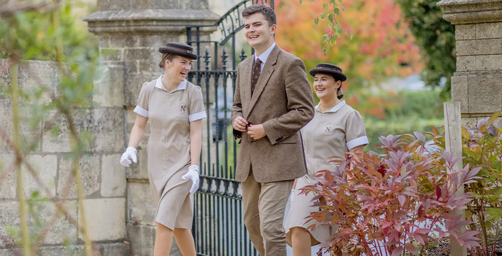 A male and two female Norland Nanny students walking through a gate at the Upper Oldfield Park campus in Bath