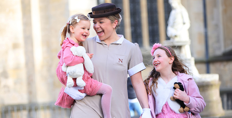 Norland Nanny in formal uniform holding hands with child