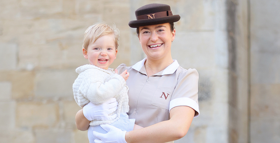 Norland Nanny in uniform holding smiling baby