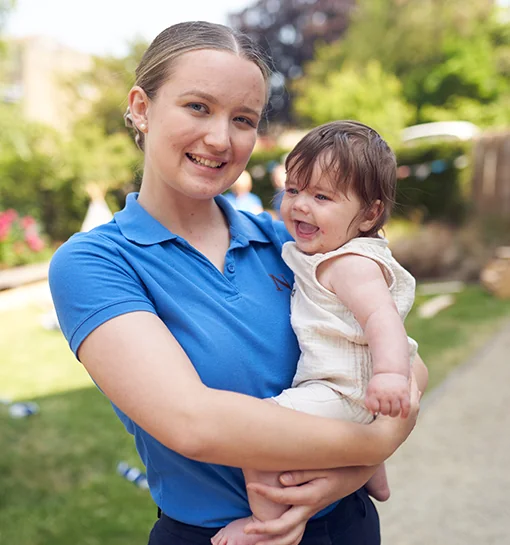 Norland student in practical uniform holding baby outdoors