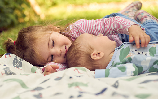 A baby led on the floor with a child hugging them