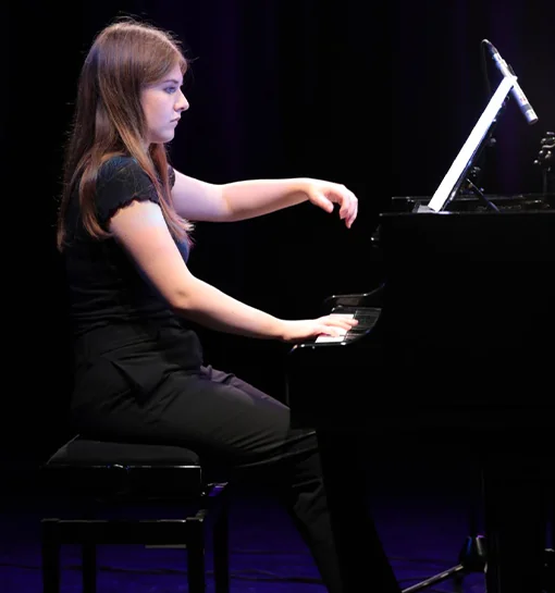 A girl playing the piano, with piano teaching one of the ways she funds her studies