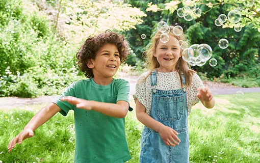 Two children in a park chasing bubbles