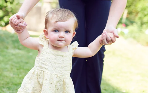 A child walking with an adult holding the child's hands
