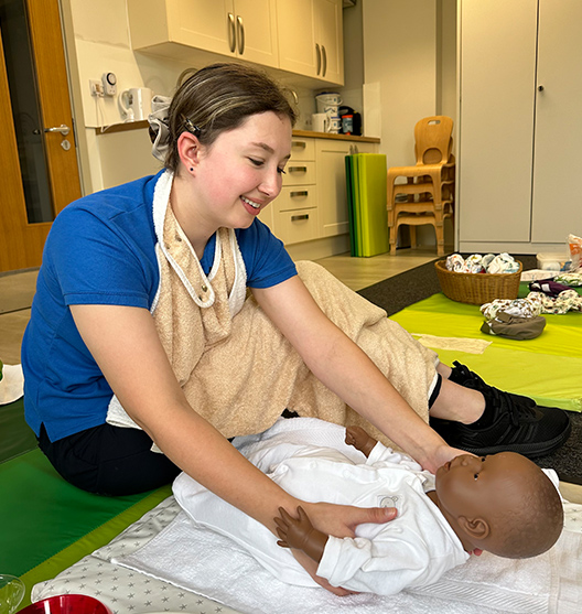 Norland student in practical uniform with virtual doll in nursery