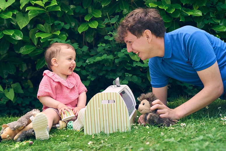 A male Norland Nanny student led on the floor playing with a smiling child